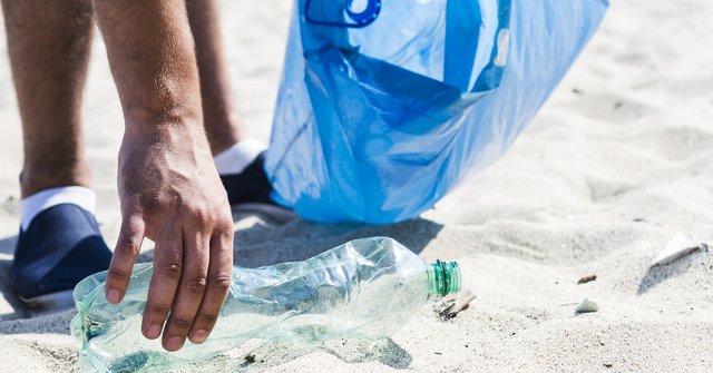 man_hand_picking_up_trash_plastic_bottle_by_beach_while_holding_blue_garbage_bag